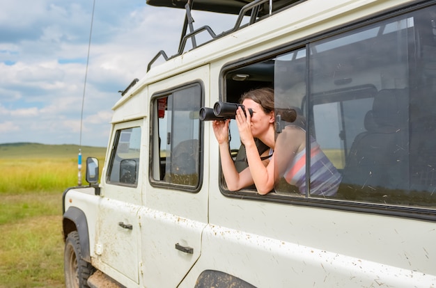 Woman tourist on safari in Africa, travel in Kenya, watching wildlife in savanna with binoculars