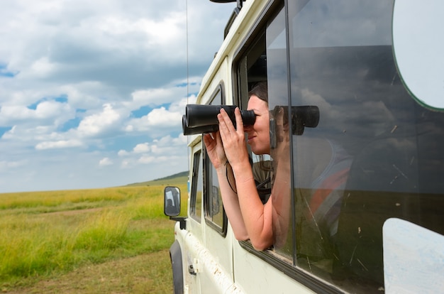 Woman tourist on safari in Africa, travel in Kenya, watching wildlife in savanna with binoculars