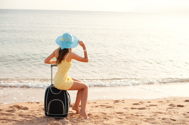 スーツケースに海のそばに座っている女性観光客