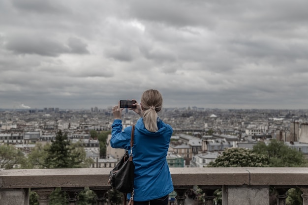 携帯スマートフォンのカメラで曇りの天気で街の写真を撮る女性観光客