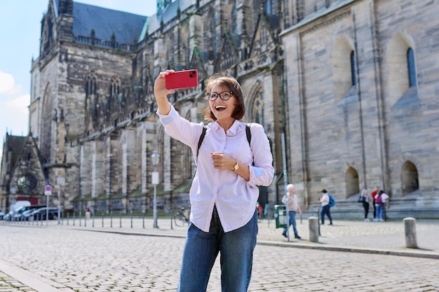 Woman tourist taking a selfie in front of an ancient European temple cathedral Female traveling through Germany using smartphone to take photo Tourism history architecture concept