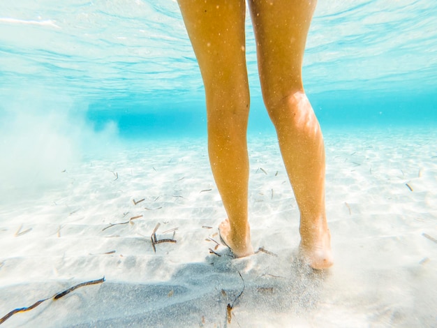 カリブ海の透明な海で柔らかい白い砂の上で水中サルキングを眺める女性観光客の足