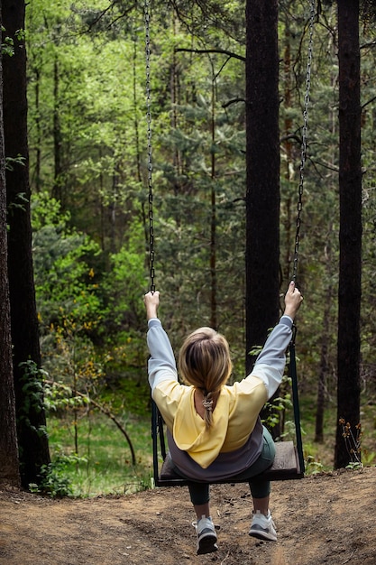 a woman tourist on a walk in a green forest rides on a high swing attached to tall trees