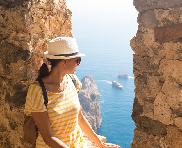 A woman tourist with a backpack and a hat sits on the fortress wall in the fortress of Alanya Turkey