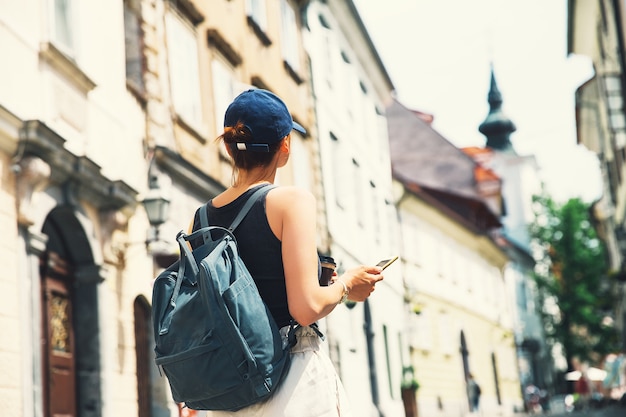 류블랴나(Ljubljana) 구시가지의 중세 거리에서 스마트 폰을 사용하여 커피 한 잔을 들고 있는 여성 관광객