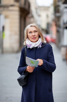 Turista della donna con una mappa in mano cammina lungo la strada.