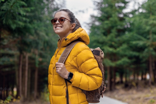 Turista donna in piumino giallo con zaino da turismo retrò in pelle fare una passeggiata nella natura backgr