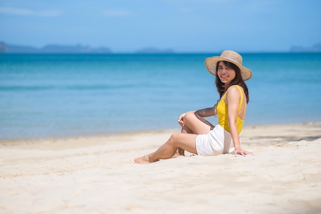 노란 수영복을 입은 여성 관광객과 모자를 쓴 행복한 여행자는 섬 목적지 방랑벽 아시아 여행 열대 여름 휴가 및 휴가 개념의 파라다이스 해변에서 일광욕을 하고 있습니다.