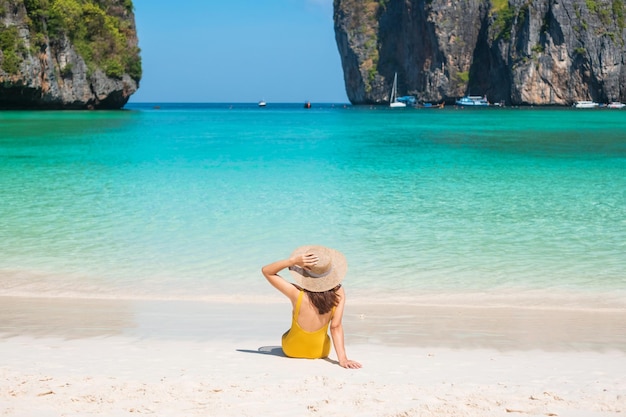 Женщина-туристка в желтом купальнике и шляпе счастливая путешественница загорает на пляже Майя-Бэй на острове Пхи-Пхи, Краби, Таиланд, достопримечательность Юго-Восточной Азии.