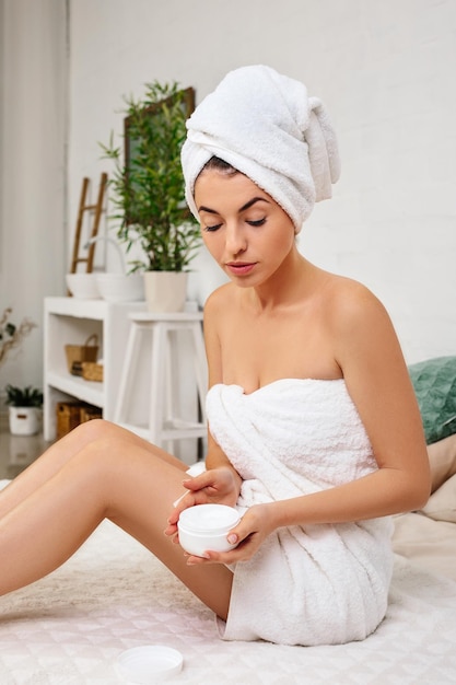 Woman in towel applying cream on her hands