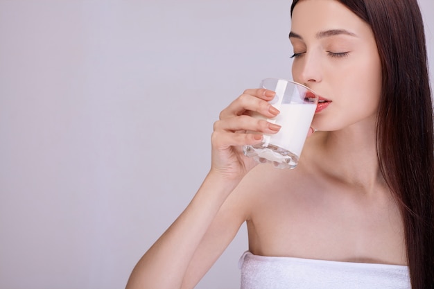 Woman in a towel drinks milk with her eyes closed