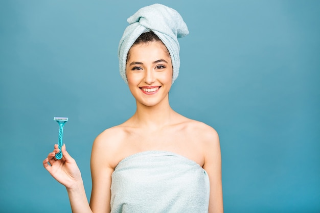 Woman in towel on head and body after shower holding manual razor, morning or evening beauty routine.