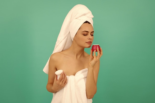 Woman in towel smell skin cream on blue background