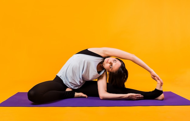 A woman in a tracksuit performs stretching on a purple Mat on an orange wall