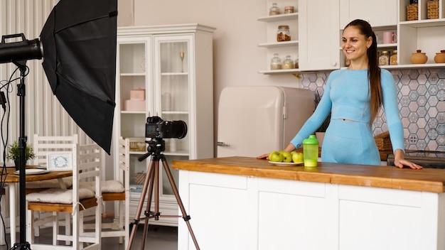 Una donna in tuta registra un video blog su sport e alimentazione sana. attrezzatura professionale nello studio fotografico con interni cucina