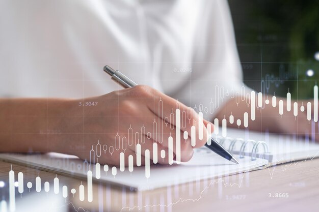 A woman trader in formal wear writing down some ideas to research stock market to proceed right investment solutions Wealth management concept Hologram Forex chart over close up shot