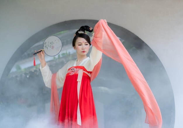 Foto donna in abiti tradizionali che tiene il ventilatore a mano contro la finestra