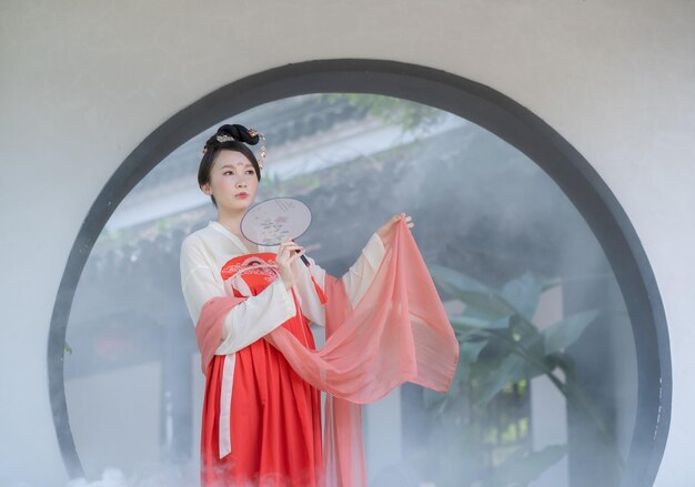 Photo woman in traditional clothing holding hand fan against window