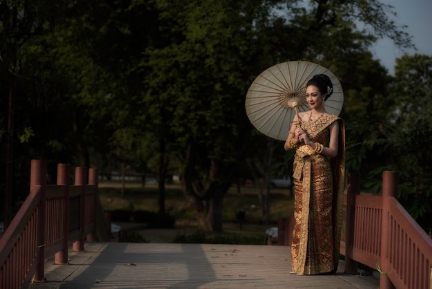 Photo woman in traditional clothing holding umbrella while standing on footbridge at park