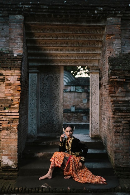 Foto donna in abiti tradizionali che guarda lontano mentre è seduta in un edificio storico