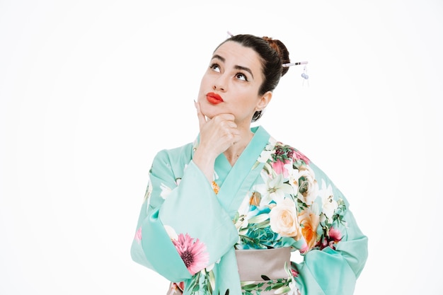 Woman in traditional japanese kimono looking up puzzled touching her chin with hand on white