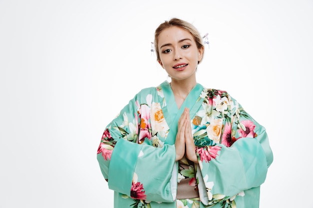 Женщина в традиционном японском кимоно улыбается, взявшись за руки в приветственном жесте на белом