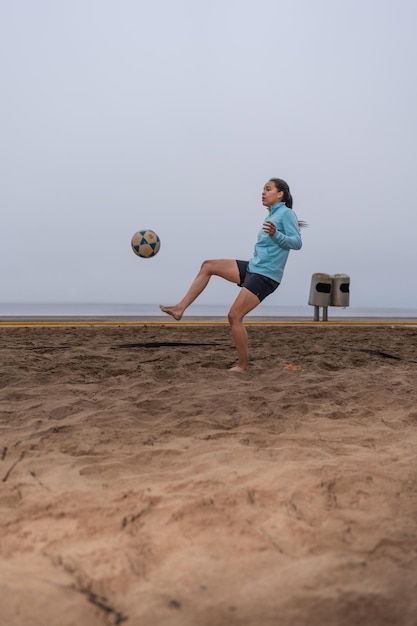 Woman training while kicking a ball on the beach