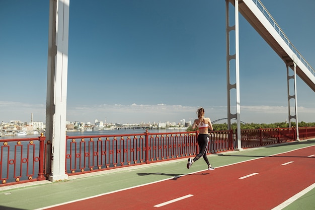 Woman trains running along road on contemporary footbridge on summer day