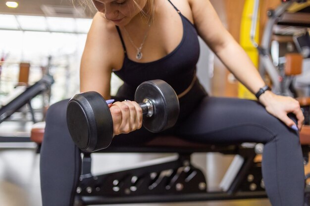 A woman trains with a dumbbell in her hand while sitting on a bench in the gym Concentrated biceps dumbbell curls