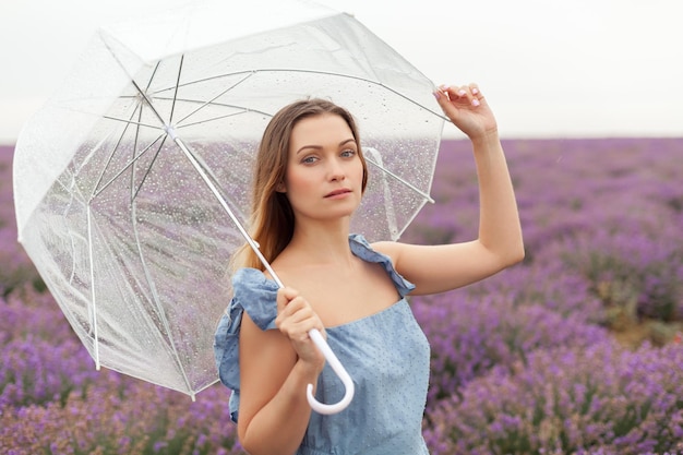 透明な傘の下の女性は、ソフト フォーカスの写真を閉じます。ラベンダー畑の雨の下