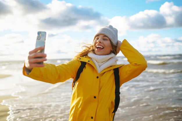 女性旅行ブロガーが海の夕暮れでソーシャルネットワークのためにセルフィーを撮ります旅行観光のリラックスコンセプト