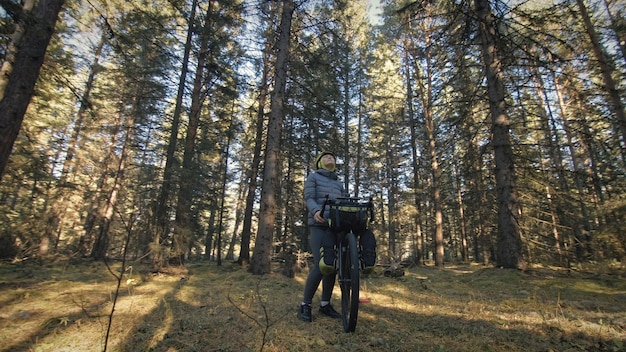 La donna viaggia su terreni misti cicloturismo con bici bikepacking outdoor il viaggiatore viaggio con borse da bici elegante bikepacking abbigliamento sportivo da bici nei colori verde nero magico parco forestale