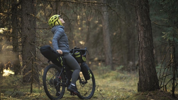 女性は屋外で自転車バイクパッキングを使って混合地形サイクルで旅行します自転車バッグを持って旅行者の旅グリーンブラックカラーのスタイリッシュな自転車パッキングバイクスポーツウェアマジックフォレストパーク