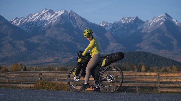 女性はバイクパッキングを使って混合地形サイクルで旅行します自転車バッグを持った旅行者の旅スポーツ観光バイクパッキング自転車スポーツウェア（緑と黒の色）山の雪をかぶった
