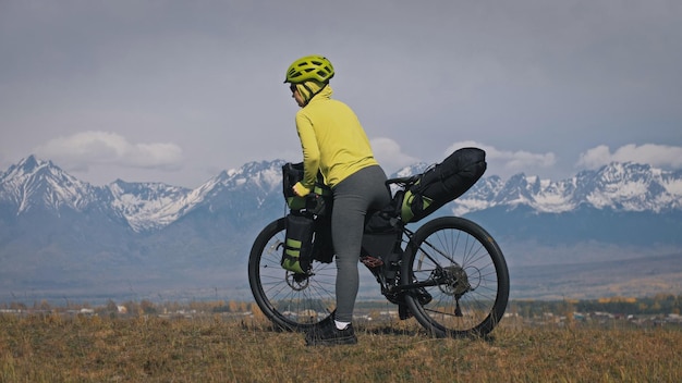 女性はバイクパッキングを使って混合地形サイクルで旅行します。自転車のバッグを持った旅行者の旅。スポーツツーリズムバイクパッキング。