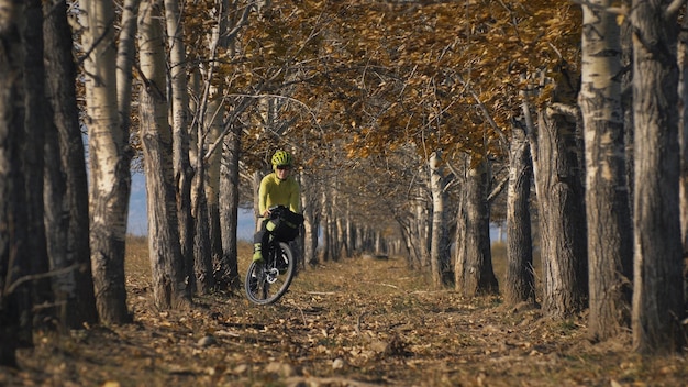 Женщина путешествует по смешанной местности, ездит на велосипеде, путешествуя с велосипедом. Путешественница с велосипедными сумками. Спортивная одежда в зелено-черных тонах. Поездка в волшебный осенний лес.