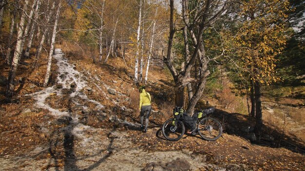 女性はバイクパッキングで混合地形サイクルを旅行します自転車バッグを持った旅行者の旅緑の黒い色のスポーツウェア魔法の秋の森の川の小川での旅行