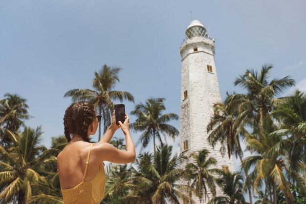 Foto donna viaggiatrice davanti al famoso punto di riferimento dello sri lanka con lo smartphone dondra lighthouse