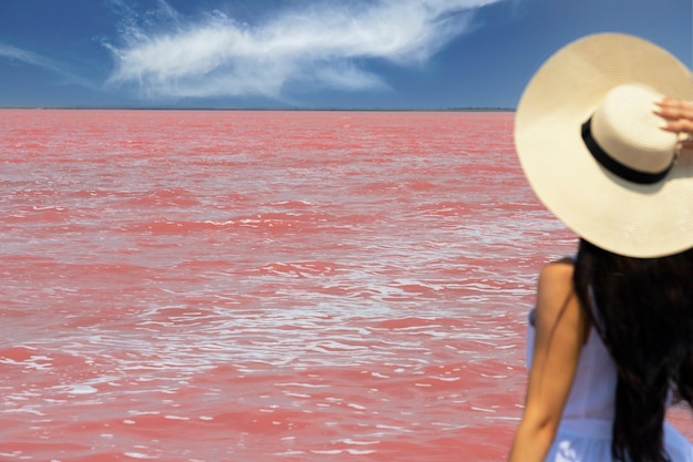 모자를 쓴 여성 여행자는 놀라운 이국적인 분홍색 소금 호수와 푸른 하늘을 봅니다. 방랑벽 여행 개념, 텍스트 복사 공간. 선택적 초점입니다. 고품질 사진