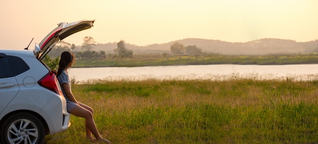 Woman traveler sitting on car Relax from the work week In the evening in the midst of nature.