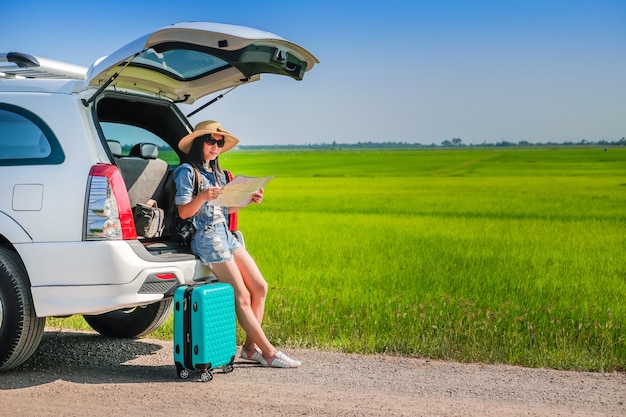 woman traveler sitting on hatchback of car and reading a map
