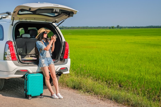 woman traveler sitting on hatchback of car and taking photo 