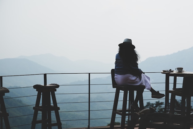 丘の上にカフェテラスの外に座って、美しい山の景色とコーヒーを飲む女性旅行者。