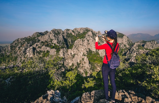 女性旅行者が立って山の頂上に写真を撮り、美しいナチュールを楽しむ