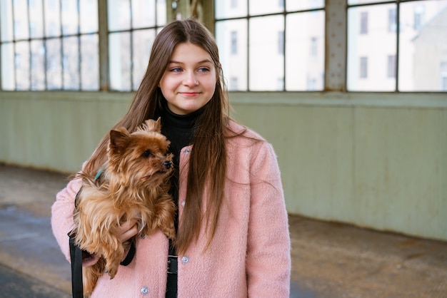 Woman traveler tourist walks with luggage and dog at train\
station in pink coat the concept of an ac...