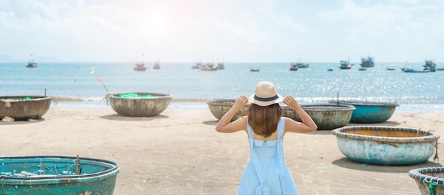 Woman traveler visiting at My Khe beach and sightseeing basket finishing boats Tourist with blue dress and hat traveling in Da Nang city Vietnam and Southeast Asia travel concept