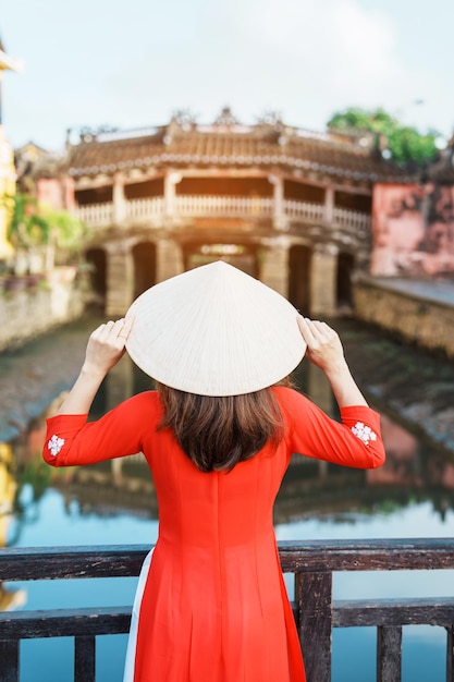 Женщина-путешественница в вьетнамском платье Ао Дай осматривает достопримечательности японского крытого моста в городе Хойан, достопримечательность Вьетнама и популярная среди туристов туристическая концепция Вьетнама и Юго-Восточной Азии