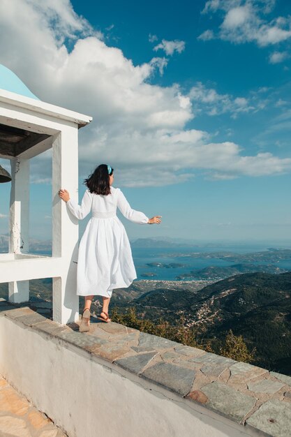 レフカダ島の風景のパノラマビューを探している白いドレスを着た女性旅行者