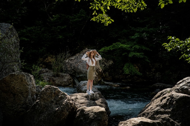 Woman traveler with backpack and hat walking in amazing mountains and forest near river with deep blue water