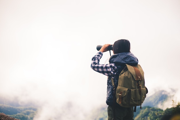 帽子を持って、驚くべき山と森を見ているバックパックを持つ女性旅行者。